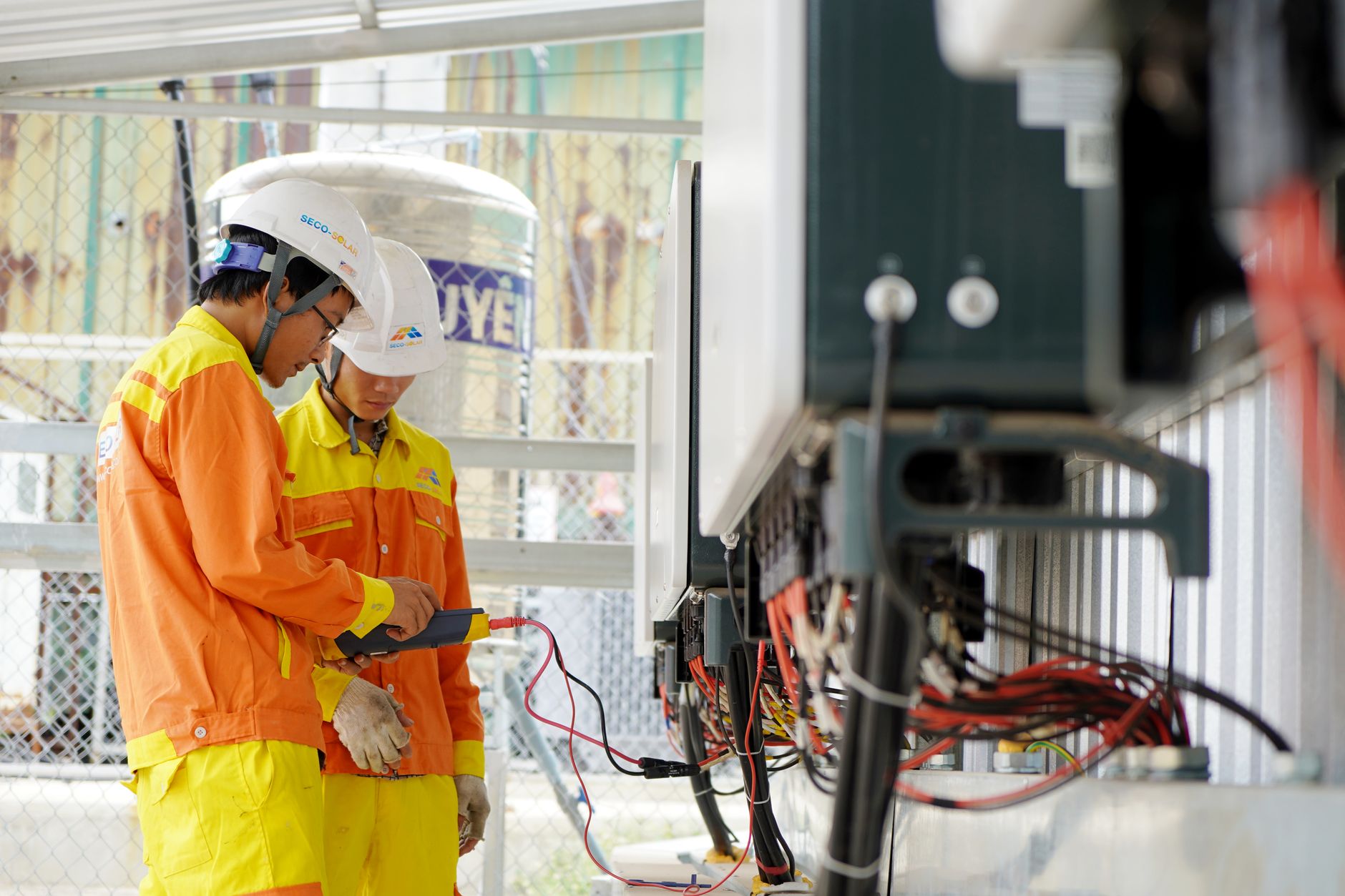 Két villanyszerelő védősisakban kültéri elektromos berendezésen dolgozik